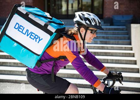 Frau im Helm mit großen Lebensmittel Lieferung Rucksack Fahrrad auf der Straße zu fahren. Sonniger Frühlingstag in der Stadt. Porträt einer Kurierin auf einem Fahrrad Stockfoto