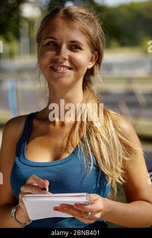 Junge schöne Mädchen schreibt etwas in ihr Notizbuch, während sie im Park steht. Stockfoto