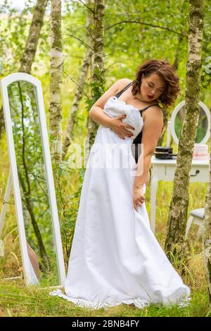 Eine Schönheit Frau versucht auf einem Hochzeitskleid vor dem Spiegel im Wald, Morgen der Braut, natürliche Schönheit Stockfoto