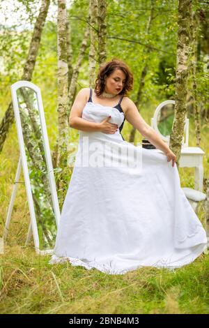 Eine Schönheit Frau versucht auf einem Hochzeitskleid vor dem Spiegel im Wald, Morgen der Braut, natürliche Schönheit Stockfoto