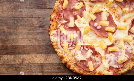 Eine hawaiianische Pizza sitzt auf einem dekorativen Schneidebrett. Stockfoto