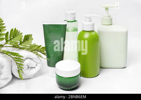 Kosmetikbehälter mit grünen Kräuterblättern und weißen Handtüchern, leeres Etikettenpaket für Branding-Mock-up. Feuchtigkeitsspendende Creme, Shampoo, Tonic, Gesicht und Stockfoto