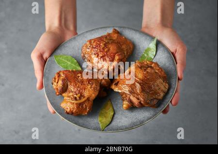 Filipino Chicken Adobo auf grauem Teller in weiblichen Händen. Chicken Adobo ist philippinische Küche Gericht aus geschmorten Hähnchenschenkel, Sojasauce, Essig, schwarzen Pfeffer Stockfoto