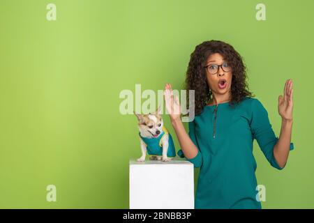 Zeigt etwas großes mit den Fingern. afroamerikanische junge Frau Porträt isoliert auf grünem Hintergrund. Schönes Modell mit wenig doggy. Konzept der menschlichen Emotionen, Gesichtsausdruck, Verkauf, Anzeige. Stockfoto
