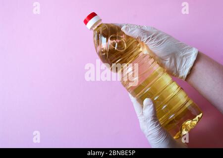 Hände halten reines Sonnenblumenöl in Plastikflasche. Gewürze für Salate. Auf rosa Hintergrund. Stockfoto