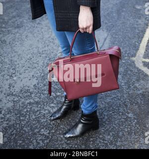 Frau mit einer kastanienbraunen Lederhandtasche in Denim und Schwarz Stiefel auf einer Straße Stockfoto