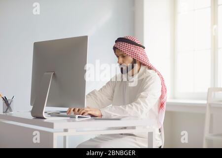 Arabischer Geschäftsmann Arbeiter mit Bart arbeitet im Computer am Arbeitsplatz im Büro. Busy ernst arabischen Mann analysiert Drucke denkt funktioniert. Stockfoto