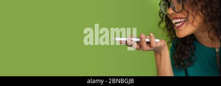 Sprachnachricht wird aufgezeichnet. afroamerikanische junge Frau Porträt isoliert auf grünem Studio Hintergrund. Schöne weibliche lockiges Modell. Konzept der menschlichen Emotionen, Gesichtsausdruck, Verkauf, Anzeige, Jugend. Stockfoto