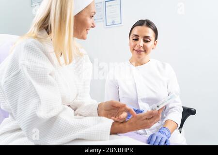 Dermatologin, die ein kosmetisches Produkt in der Hand ihres Patienten betrachtet Stockfoto