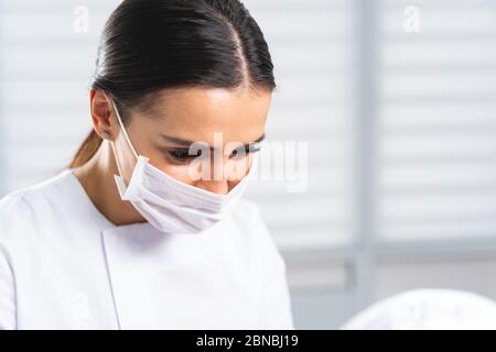 Frau in einer Gesichtsmaske, die ein kosmetisches Verfahren durchführt Stockfoto