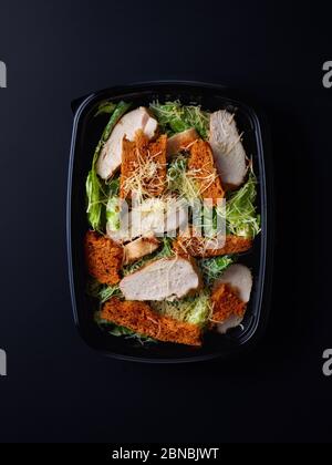 Caesar Salat in schwarzer Kunststoffbox zum Mitnehmen, auf schwarzem Hintergrund, Draufsicht Stockfoto
