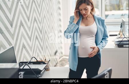 Gestörte schwangere Dame, die im Büro auf dem Handy spricht Stockfoto