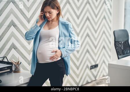 Verärgert schwangere Frau, die im Büro auf dem Handy spricht Stockfoto