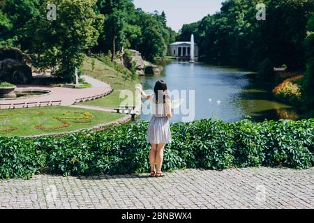 Sofia Park, Ukraine. Junge Frau mit einer touristischen Karte Spaziergänge in einem Landschaftsgarten. Mädchen mit einer touristischen Karte auf dem Hintergrund des Sees mit einem Brunnen. Stockfoto