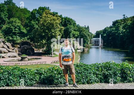 Sofia Park, Ukraine. Schöner Mann mit Bart in einem dendrologischen Park. Mann mit Rucksack auf dem Hintergrund des Sees mit einem Brunnen und einem weißen Stockfoto