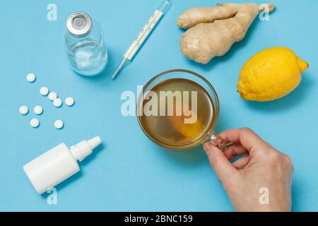 Nasenspray, Pillen, eine Glasflasche, ein Quecksilberthermometer, eine weibliche Hand mit einer Tasse Tee, Zitrone und Ingwer. Draufsicht. Konzept des Behandlungskits. Gesundheit r Stockfoto