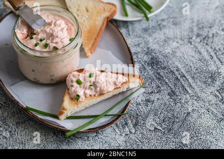 Lachs und weicher Cremekäse im Glas. Lachsrilletten, Mousse, Pastete und Toasts auf grauem Hintergrund Stockfoto