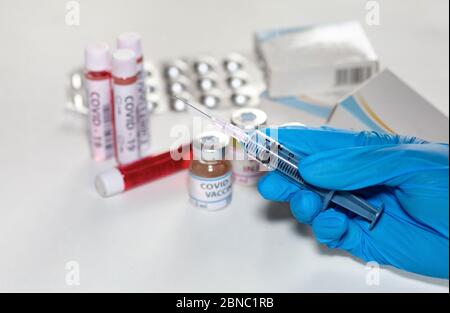 Hände eines Arztes in medizinischen Handschuhen, die eine hypodermische Nadel halten, die Medikamente aus einer Impfstoffflasche mit Blick auf Arzneimittel und Blutproben injiziert Stockfoto