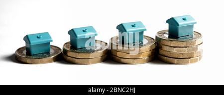 Kleine blaue Häuser auf Stapeln von 1 Pfund Münzen vor weißem Hintergrund. Wachstumskonzept Stockfoto