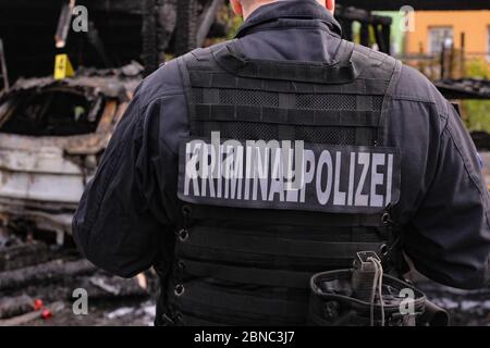 Dresden, Deutschland. Mai 2020. Der Ermittler der Brandursache mit der Aufschrift 'Kriminalpolizei' auf dem Rücken befindet sich in einem Ausschnitt auf der rechten Seite des Bildes. Im Hintergrund des Bildes links befindet sich eine forensische Plakette auf dem Dach eines ausgebrannten Autos in der Unschärfe.Quelle: Tino Plunert/dpa-Zentralbild/ZB/dpa/Alamy Live News Stockfoto