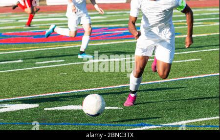 High School Jungen Fußballspiel mit einem Sportler jagen th eball auf dem Feld trägt eine weiße Uniform. Stockfoto