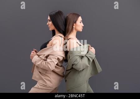 Fashion Portrait von zwei attraktiven Business-Frauen in Anzügen und Tops posiert auf grauem Hintergrund Stockfoto
