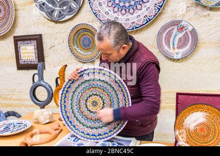 Türkische Ladenbesitzer, die die traditionellen Keramikbecher und -Gläser in einem unterirdischen Keramikgeschäft in Avanos, Kappadokien, Türkei, vorstellen. Stockfoto