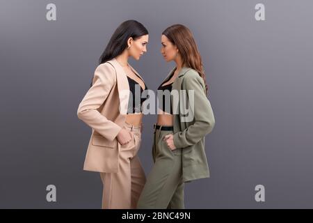 Fashion Portrait von zwei attraktiven Business-Frauen in Anzügen und Tops posiert auf grauem Hintergrund. Streit Stockfoto