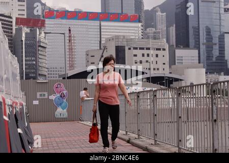 Hongkong, CHINA. Mai 2020. Frau Spaziergang entlang der Strandpromenade außerhalb CONVENTION CENTER in Wan Chai, hinter sehen Sie ein mobiles Display zeigt Bild von mehreren Nationalflaggen der VR China.Pro-Peking Gesetzgeber werden erwartet, zu fördern und die Gesetzgebung der umstrittenen NATIONALEN FLAGGE GESETZ am HKSAR Legislative Council am 27. Mai diesen Monats.14. Mai 2020 Hong Kong.ZUMA/Liau Chung-ren Quelle: Liau Chung-ren/ZUMA Wire/Alamy Live News Stockfoto