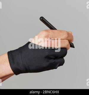 Nahaufnahme eines kaukasischen Mannes, der einen schwarzen Zweifingerhandschuh trägt und dabei einen Grafikstift in der Hand hält, auf grauem Hintergrund Stockfoto