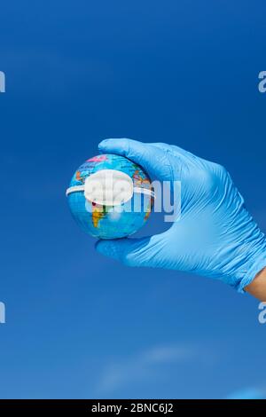 Nahaufnahme eines Mannes, der blaue Operationshandschuhe trägt, einen Erdglobus mit einer Schutzmaske hält, der die globale Coronavirus-Pandemie oder das A darstellt Stockfoto