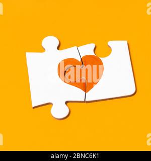 Nahaufnahme von zwei Puzzleteilen, die ein oranges Herz bilden, zur Unterstützung von Menschen, die von Multipler Sklerose betroffen sind, auf einem orangefarbenen Hintergrund Stockfoto