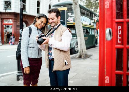 Glücklich Reisen Paar Überprüfung Fotos auf ihrer Kamera in London, Großbritannien. Doppeldeckerbus und rote Telefonzelle in einem Rahmen Stockfoto