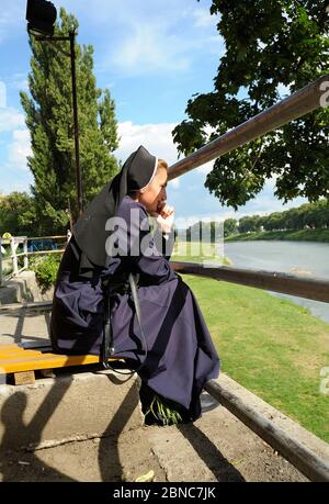 Junge Nonne auf einer Bank am Ufer des Flusses und Blick auf den Fluss UZH Stockfoto