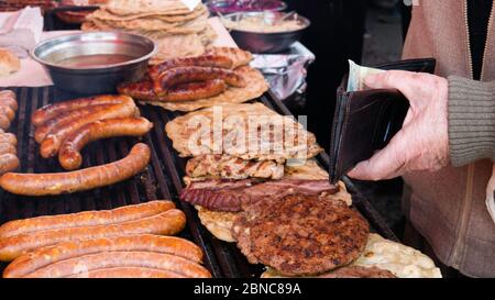 Der alte Mann hält eine Brieftasche mit 500 serbischen Dinar beim Kauf von gegrilltem Fleisch. Stockfoto