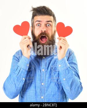Hipster in der Liebe, mit überraschten oder schockierten Gesicht feiern Valentinstag, isoliert auf weißem Hintergrund. Mann mit Bart hält rote Papierherzen oder valentinskarten in den Händen. Verrückt in Liebe Konzept. Stockfoto