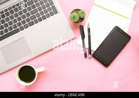 Rosa Schreibtisch mit Laptop, Smartphone, Notebook, Tasse Kaffee und Kaktus. Draufsicht Stockfoto