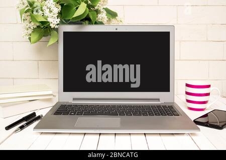 Moderner Schreibtisch mit Laptop, Smartphone, Büchern, Kaffee und Blumen Stockfoto