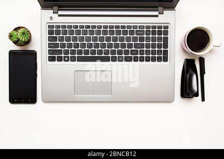 Schreibtisch mit Laptop, Smartphone, stamler und einer Tasse Kaffee und Kaktus. Draufsicht. Stockfoto