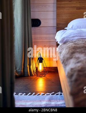 Moderne Einrichtung eines gemütlichen Schlafzimmers im Hotel mit glühender Loftlampe auf dem Holzboden
