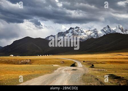 Schöne Landschaft mit weißen Gipfeln Berge, Straße und Jurtenlager im Tal in der Nähe des Kel Suu Lake in der Naryn-Region, Kirgisistan Stockfoto