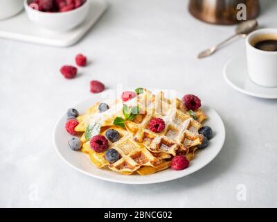 Belgische Waffeln mit Himbeeren, Heidelbeeren, Quark und Kaffee Stockfoto