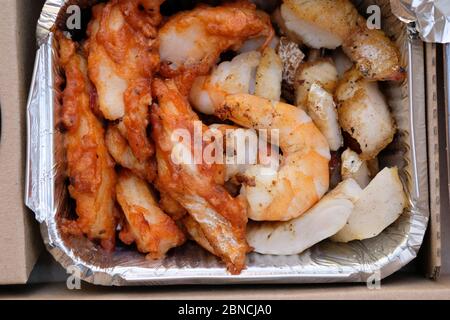 Garnelen und Fischscheiben in einem Aluminiumbehälter. Kabeljau-Fisch im Teig und Riesengarnelen von oben. Hauslieferzeit Mahlzeit mit Meeresfrüchten. Stockfoto