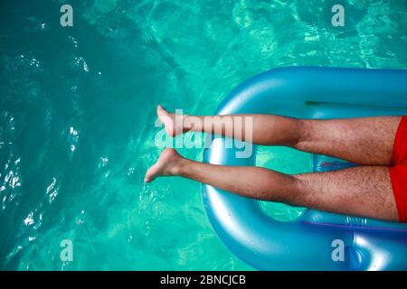 Sonnenbaden im Pool - Draufsicht auf einen halben Körper eines Mannes auf einer aufblasbaren Matratze im Pool Stockfoto
