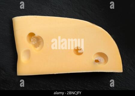 Ein Stück Hartkäse mit großen Löchern auf schwarzem Hintergrund. Gelbe Käsestücke Nahaufnahme. Stockfoto