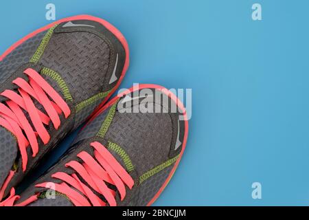 Graue Sneaker mit rosa Schnürsenkeln auf blauem Hintergrund von oben. Textil-Sneaker mit bunten Schnürsenkeln und rosa Sohlen. Das Konzept eines aktiven Lebensstils, Stockfoto