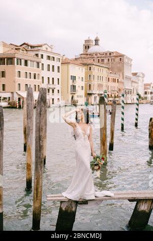 Italien Hochzeit in Venedig. Die Braut steht auf einem hölzernen Pier für Boote und Gondeln, nahe den gestreiften grünen und weißen Festmacherstangen, gegen Stockfoto