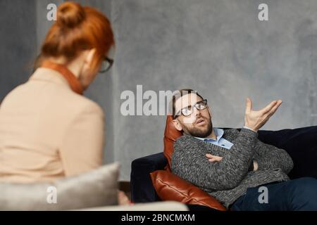 Junger Mann, der auf dem Sofa liegt und während seines Besuchs mit dem Psychologen über sein Problem spricht Stockfoto