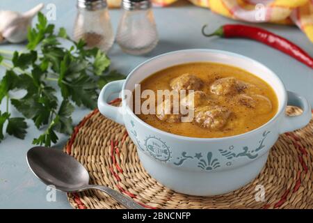 Kürbis-Sahne-Suppe mit Fleischbällchen in Schüssel auf hellblauem Hintergrund, Horizontal-Format Stockfoto