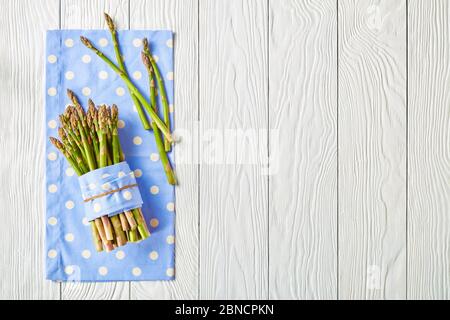Ein Bund frischer grüner Spargel auf einer blauen Serviette auf einem weißen Holztisch, flach gelegt, Freiraum Stockfoto